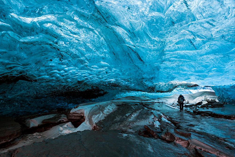 Visiteur dans une grotte de glace aux parois bleues