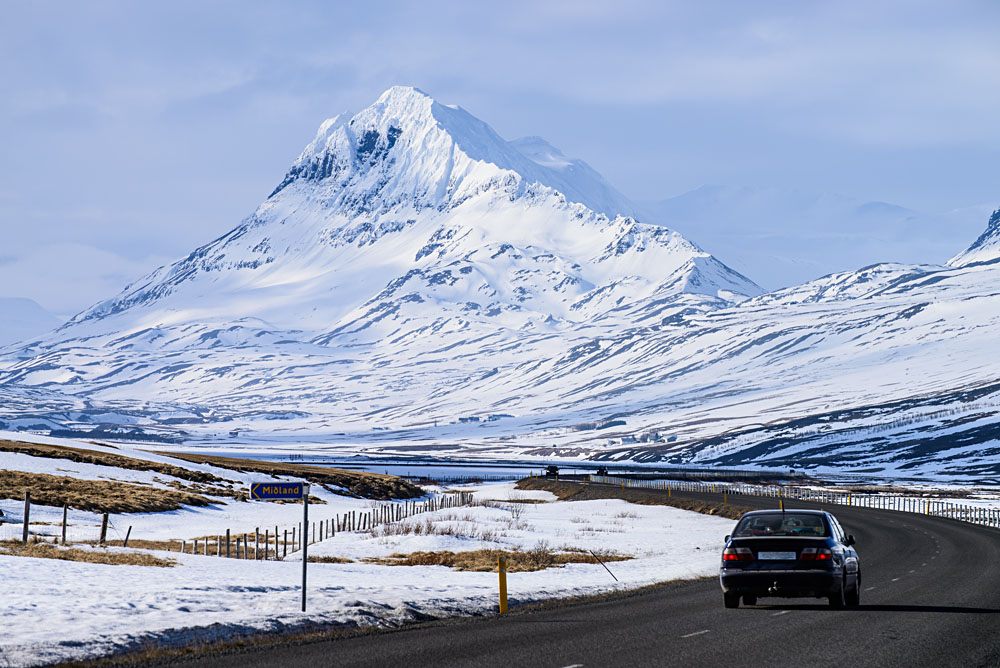 Voiture sur une route dégagée au pied de montagnes enneigées